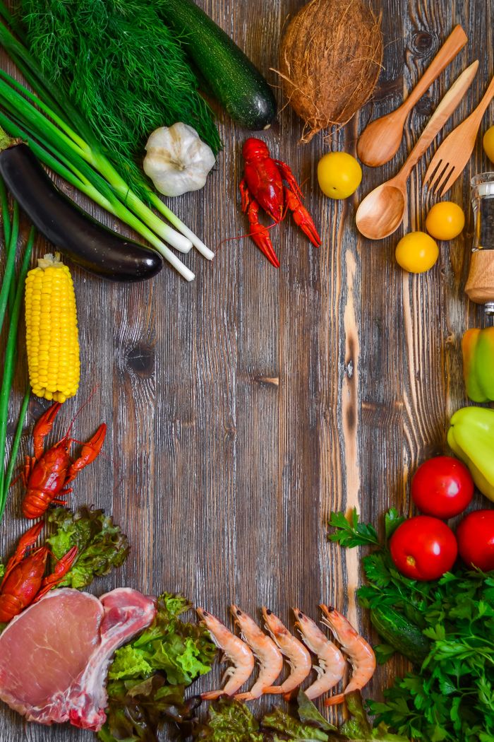 Colorful fresh ingredients including vegetables, seafood, and herbs arranged on a rustic wooden table.