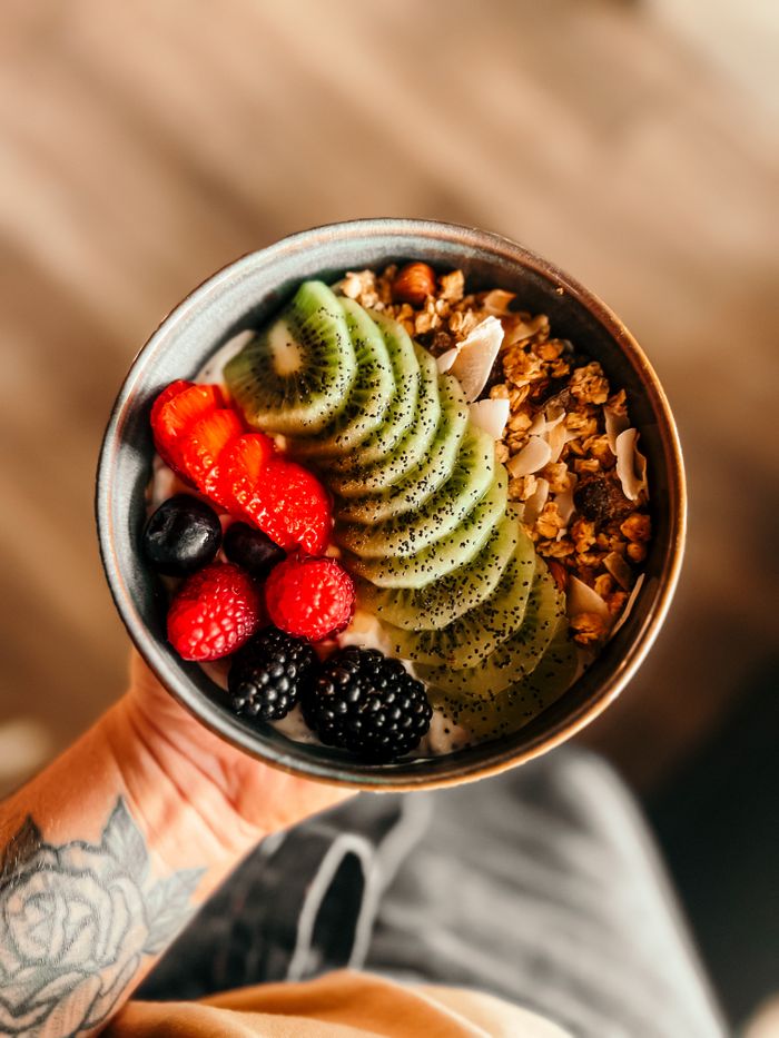 Close-up of a colorful fruit and granola bowl held by a tattooed hand.